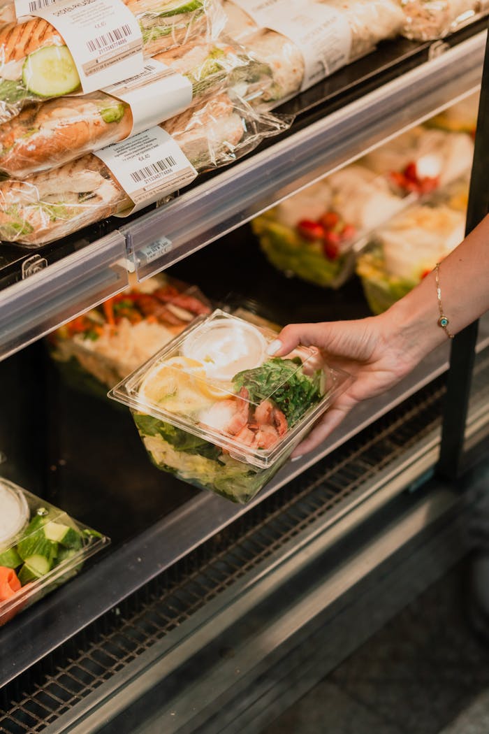 services-02 Close-up of a hand picking a packaged salad from a refrigerated display in a grocery store.