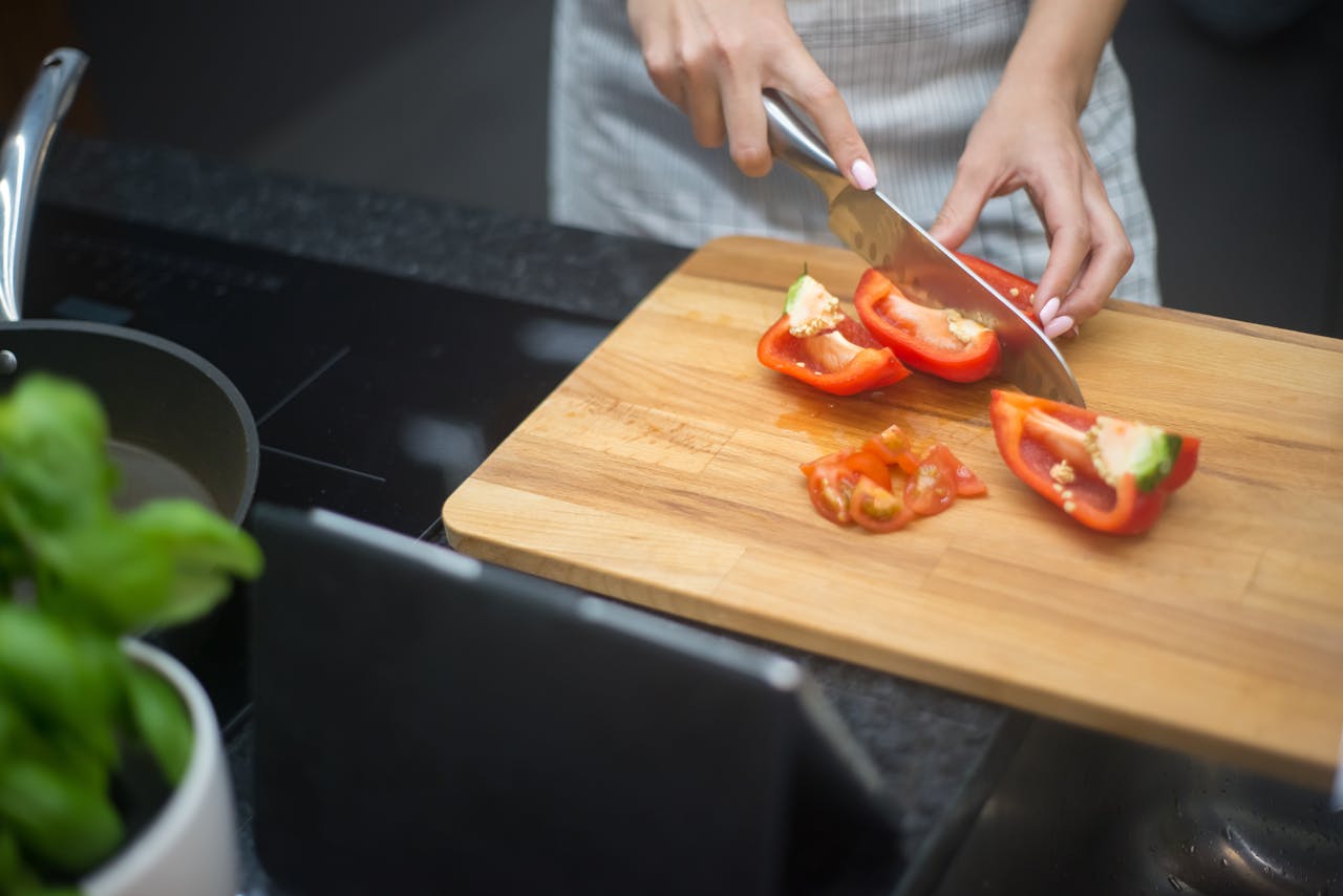 services-03 Close-up of a woman slicing red bell pepper in a modern kitchen setting.